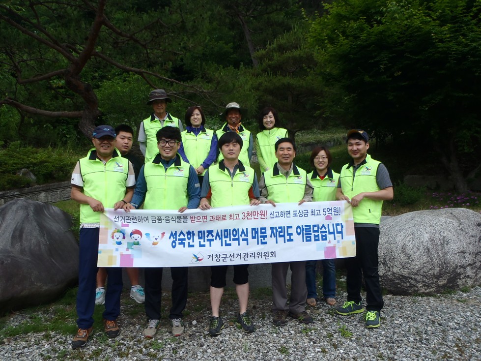 거창군 마리면 취우령 등반길에서 직원, 사회복무요원, 공정선거지원단 등이 상시 기부행위 금지 및 자연호보를 위한 현수막을 들고 서 있는 모습입니다. 자연보호를 위한 활동의 일환으로 등반길 주변에 쓰레기를 줍고 있는 모습입니다.