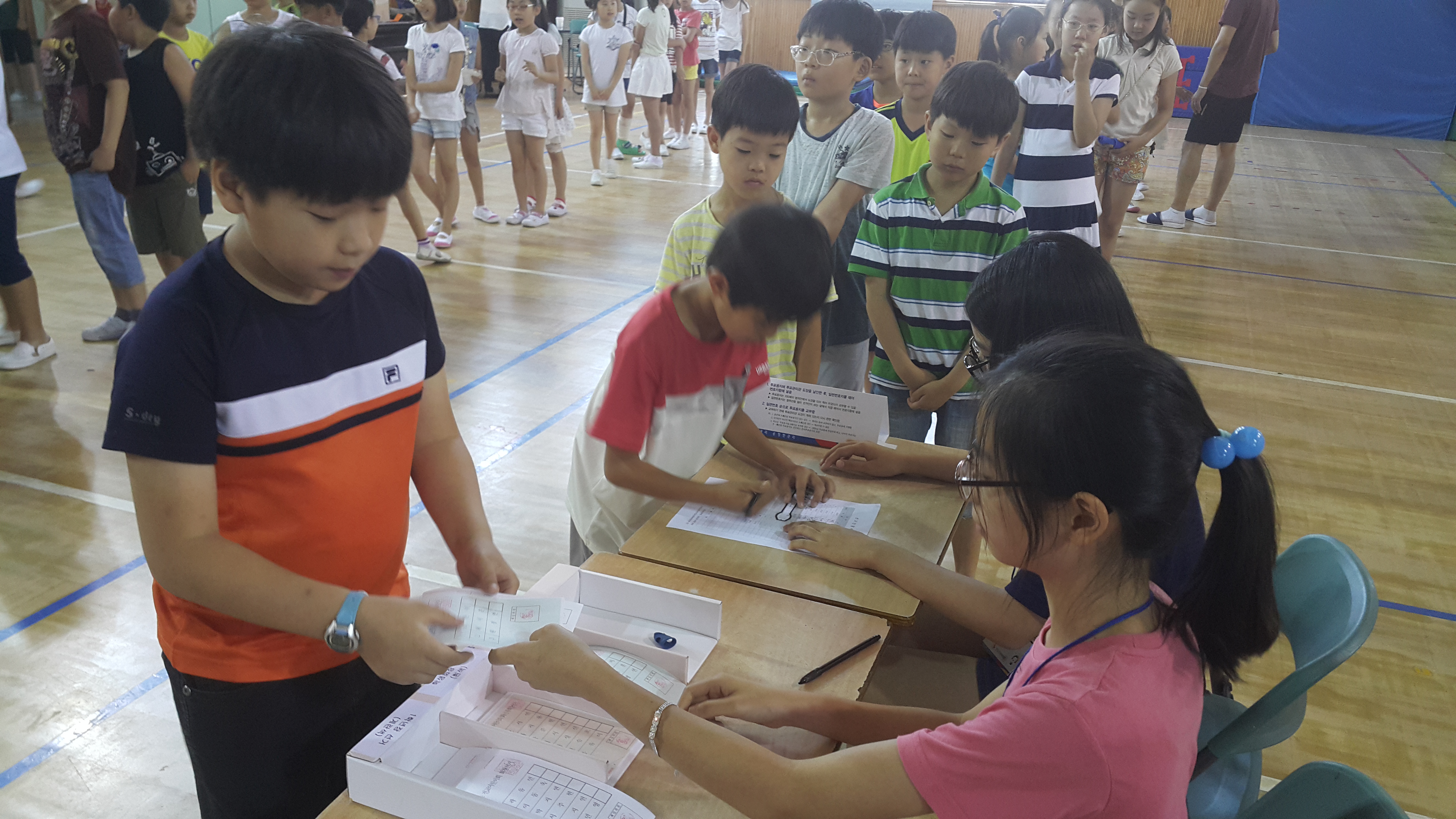 독정초등학교 학생들이 본인확인석에서 본인확인 후 투표용지를 수령하고 있는 모습의 사진입니다.