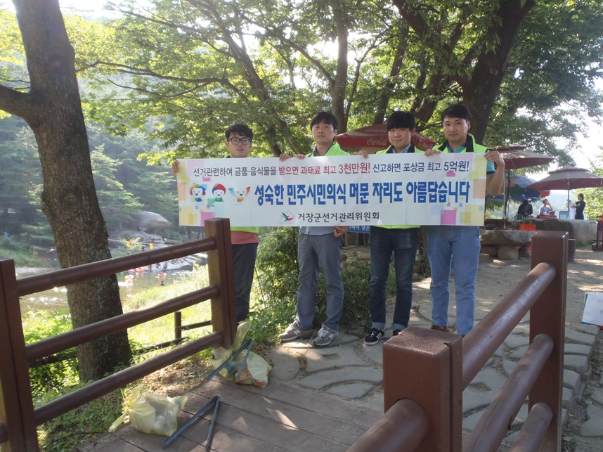 거창군선거관리위원회 직원 및 사회복무요원이 홍보용 현수막을 들고 있는 사진입니다. 
