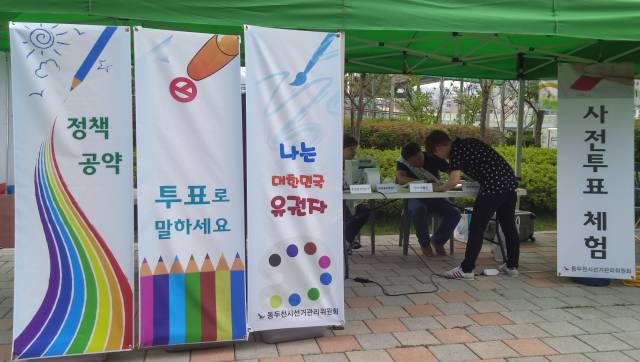 이미지 내용은 ' 정책공약, 투표로 말하세요, 나는 대한민국 유권자, 사전투표 체험'라는 내용의 배너(4종) 와 사전투표운영장비를 설치한 선거체험부스에서 사전투표 체험을 위해 본인확인기에 서명을 하는 시민의 모습입니다.
