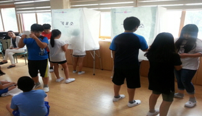투표용지를 교부 받고 기표소 앞에서 투표하기 위하여 줄을 서고 있는 학생들의 모습입니다.