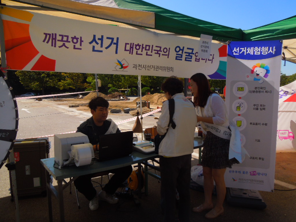 시민들이 바로마켓 장터 홍보부스에서 본인확인기와 투표용지발급기를 이용하여 선거체험을 하는 모습