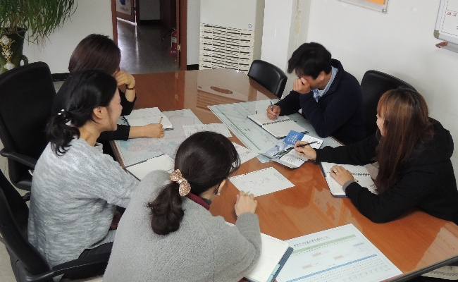 직원들과 테이블에 둘러앉아 동영상 콘티에 관하여 회의를 하는 장면