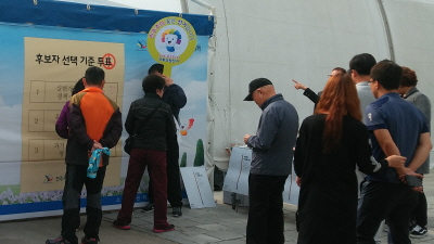 후보자 선택 기준 투표라고 써 있는 벽면 현수막에 사람들이 줄을 서서 스티커를 이용하여 투표하고 있는 모습