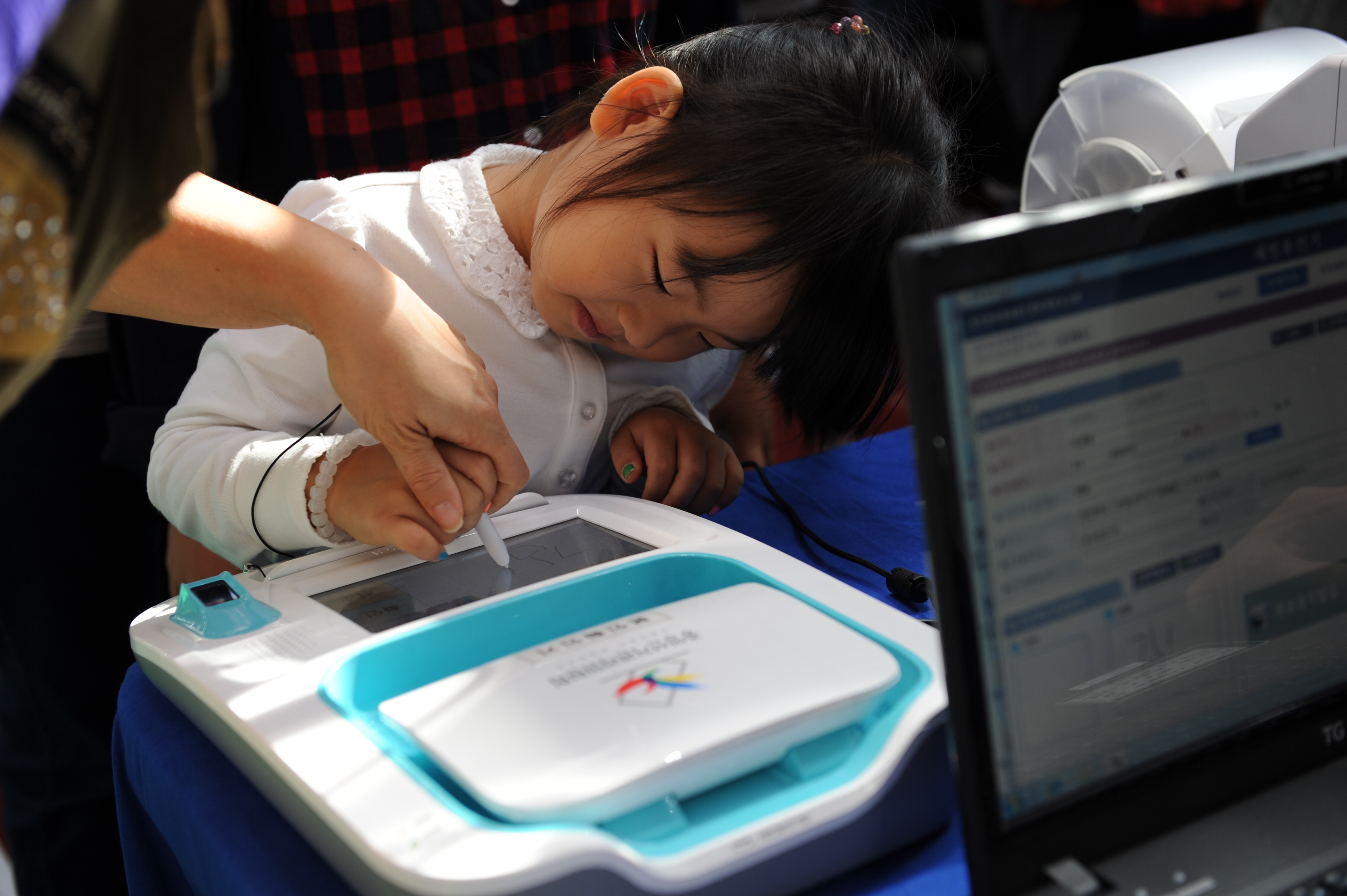 어린아이가 본인확인기에 서명하고 있는 모습