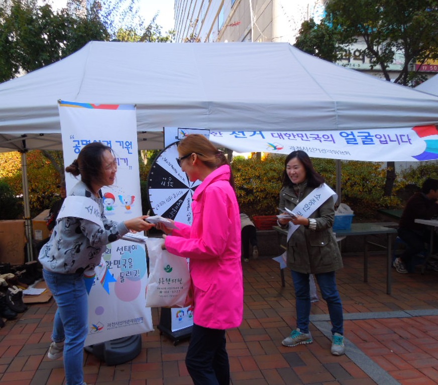 선거관리위원회 홍보주임이 룰렛돌리기 행사에 참여한 시민에게 리플릿을 배부하며 정치후원금 제도에 대해 안내하는 모습