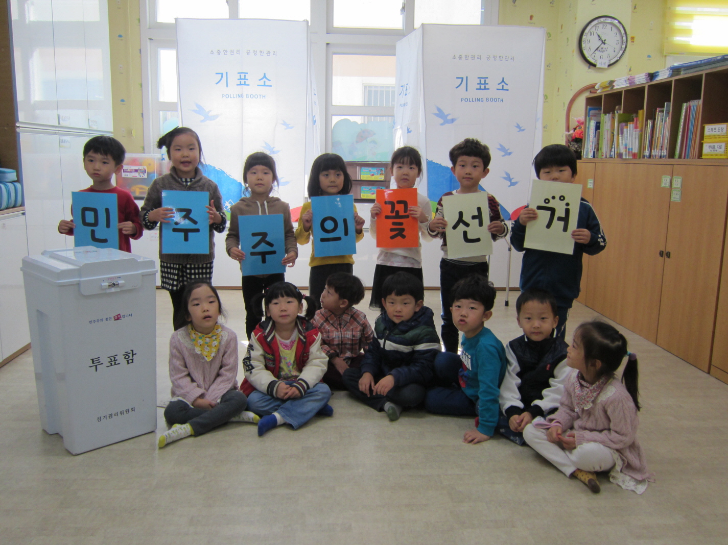 민주주의 꽃 선거 카드를 들고 기표대 앞에서 기념촬영을 하고 있습니다.