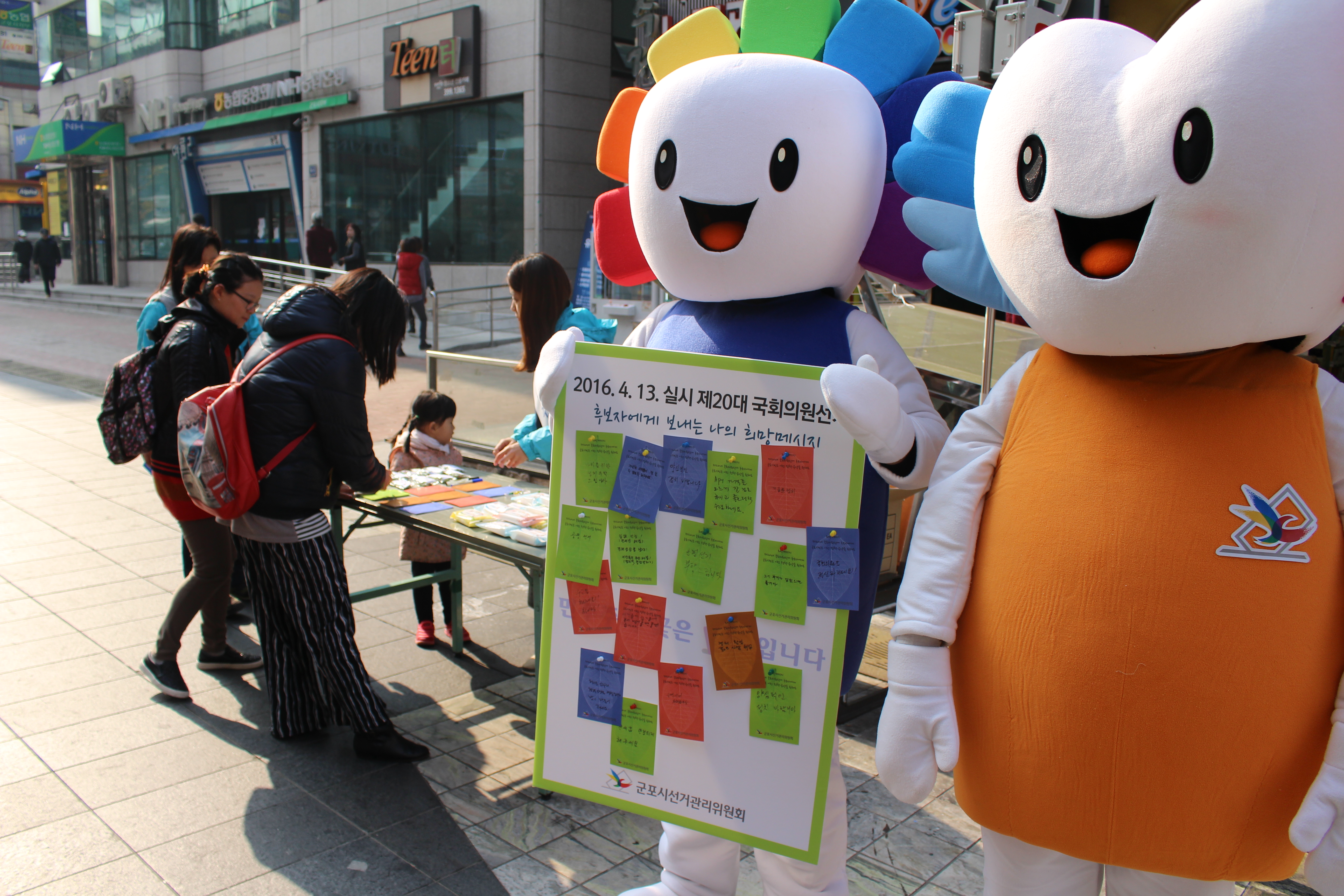 국회의원선거 후보자에게 바라는 희망메시지 적기 캠페인에 참여하고 있는 시민들의 모습과 위원회 캐릭터 참참이와 알리가 희망메시지 적기 보드판을 들고 시민들의 참여를 독려하고 있는 모습의 사진입니다.