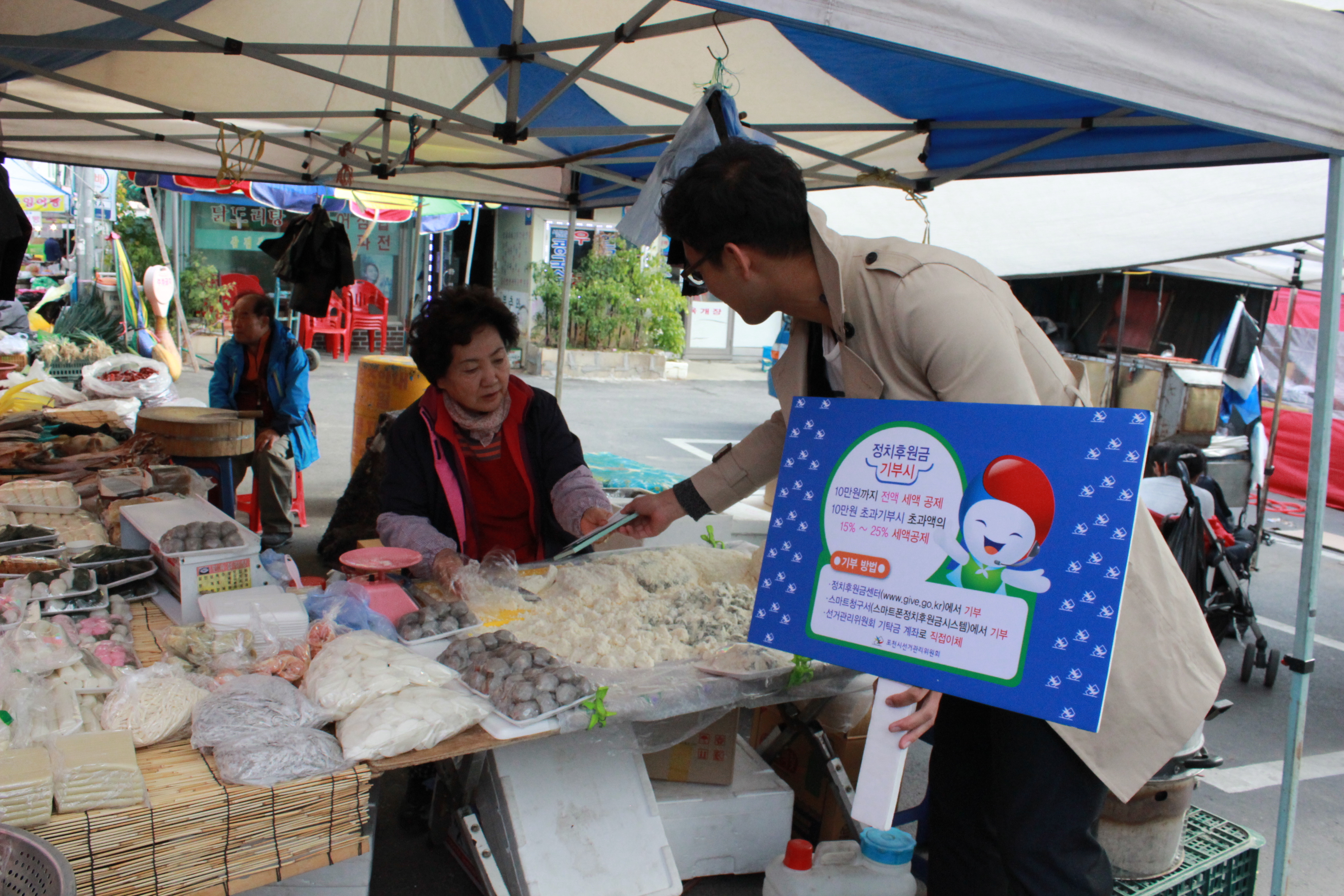 위원회 직원이 전통시장 상인분에게 정치후원금 홍보리플릿 및 홍보용품 전달하는 모습