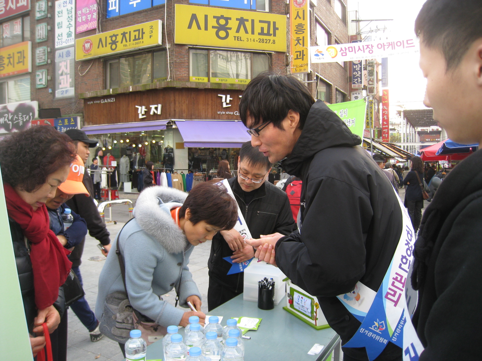 시흥시위원회 직원들이 삼미시장에서 시민들을 대상으로 미소약 엽서 캠페인을 실시하고 있는 모습