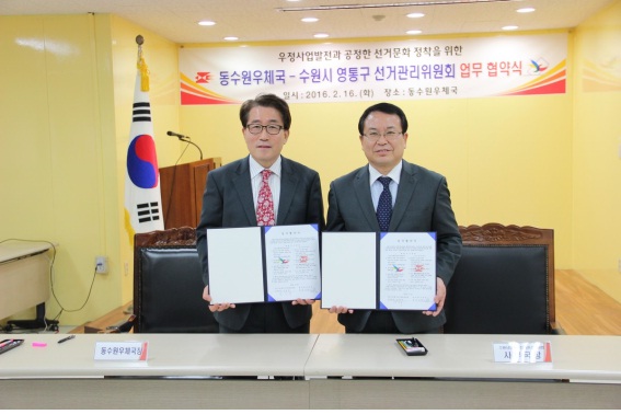 수원시영통구선거관리위원회 사무국장과 동수원우체국 총괄국장이 업무협약서를 들고 기념촬영을 하는 모습입니다.